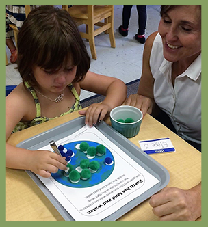 Teacher helps a student with a pom pom project